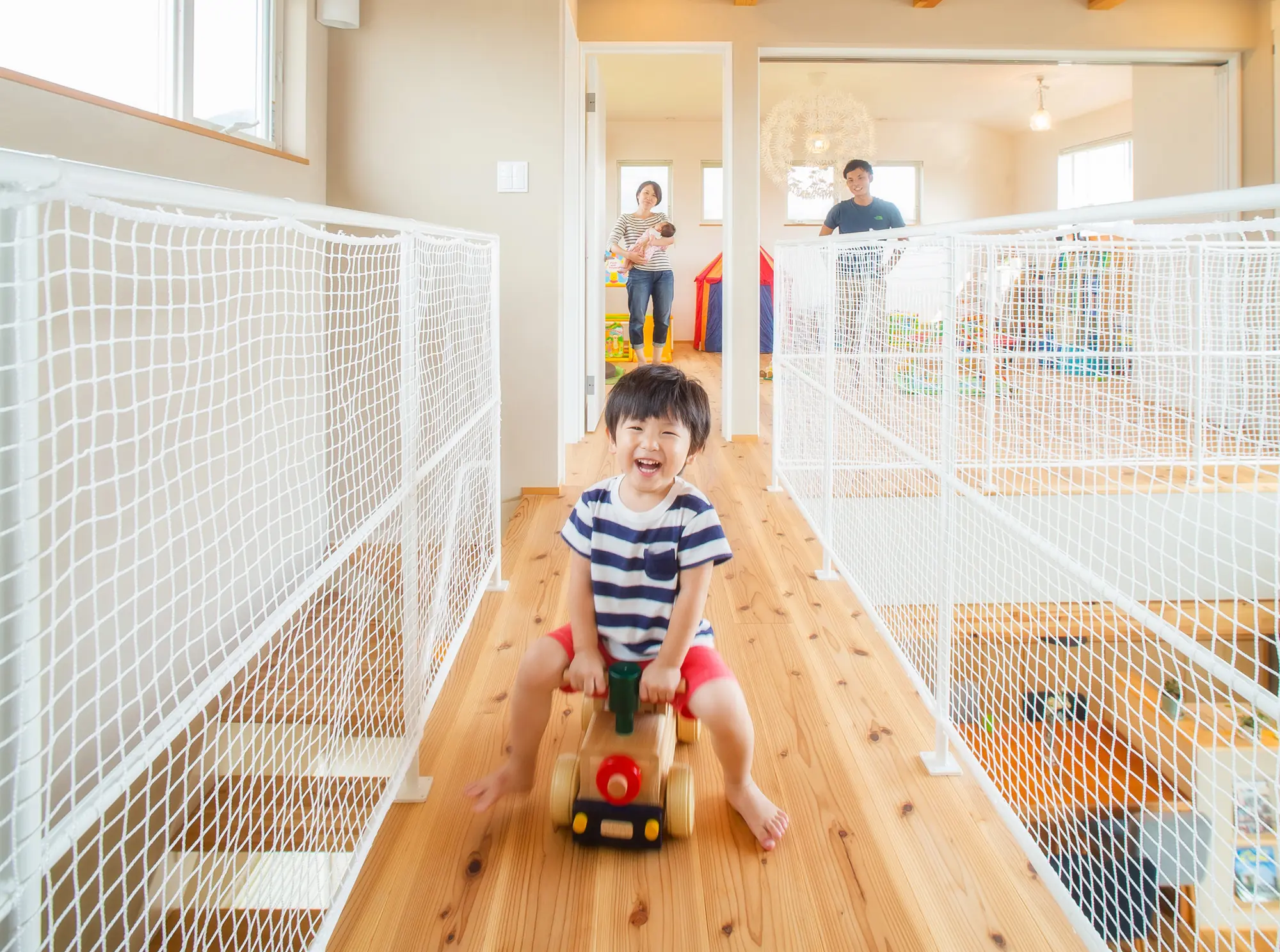 吹き抜けの廊下で木の乗り物に乗る子どもと家族