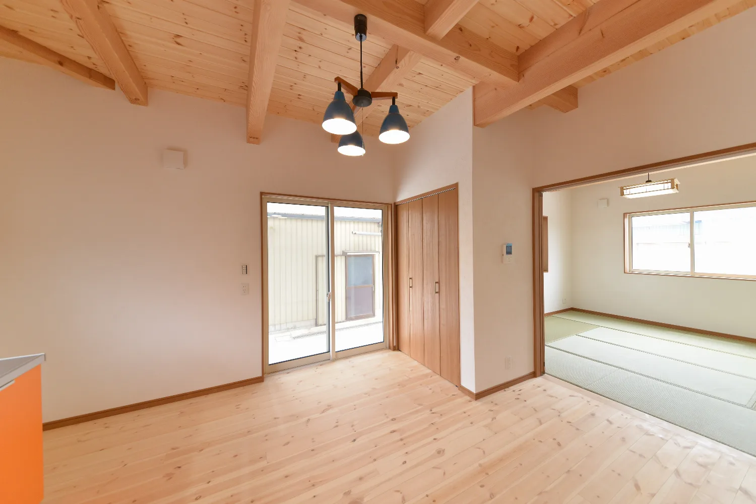 太い梁とオレンジのキッチン。和室が並ぶ、大屋根の家